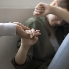 Dłoń wyciągnięta do osoby skulonej, zakrywającej twarz.