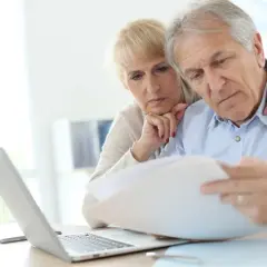 Zmartwieni seniorzy analizują dokumenty dotyczące emerytury pomostowej przy laptopie.