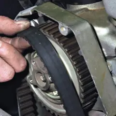 Dłoń mechanika sprawdza stan paska rozrządu przy kole zębatym silnika.