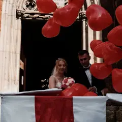 Para młoda wychodzi z kościoła, a rodzice przygotowali niespodziankę: mnóstwo czerwonych balonów w kształcie serc.