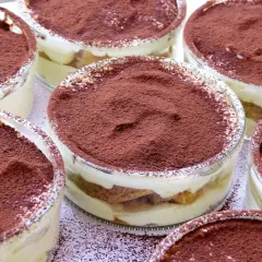 Varios vasitos de tiramisú, con capas de crema y bizcocho, espolvoreados con cacao. Los tiramisú ingredientes se ven deliciosos.