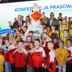 Uśmiechnięte dzieci i duża maskotka z logo lekkoatletycznych mistrzostw świata. Wszyscy pozują do zdjęcia, w tle napis "Konferencja prasowa".