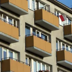 Budynek z balkonami, na jednym flaga Polski. Zastanawiasz się, ile trzeba zarabiać, aby dostać mieszkanie komunalne?