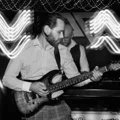 Muzyk gra na gitarze elektrycznej. Efekt świetlny na zdjęciu to długie naświetlanie, które pokazuje ruch świateł. Ekspozycja co to? To czas, przez który matryca aparatu jest naświetlana.
