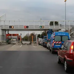 Voiture rouge et camions bleus dans une file d'attente au péage flux libre A13. Lumières rouges et vertes sur les panneaux.