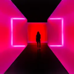 Kobieta stoi w korytarzu z neonowym oświetleniem. To nowoczesne instalacje artystyczne, które tworzą hipnotyzującą grę światła i koloru.