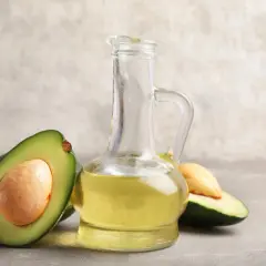 Bouteille en verre remplie d'huile avocat dorée, avec des moitiés d'avocat frais autour.