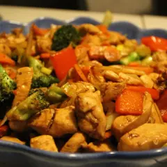 En blå skål fylld med wokad kyckling, broccoli, paprika och morötter. En läcker och färgstark måltid.