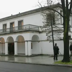 Biała willa z arkadami, gdzie mieszka Donald Tusk. Na zewnątrz widać kilka osób i drzewa.