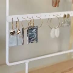 Un porta pendientes blanco exhibe varios pares de aretes colgantes, algunos con detalles dorados y otros con diseños marmoleados.