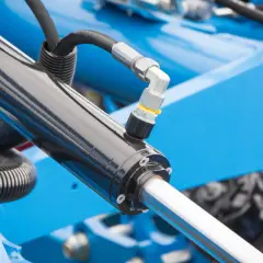 Części do hydroforu: czarny siłownik hydrauliczny z metalowym złączem i wężem, na tle niebieskiej maszyny.