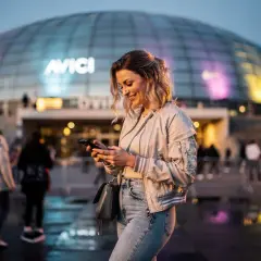 Glad kvinna med mobil framför Avicii Arena, Stockholm. Kanske väntar på en kyrkokonsert i Stockholm?