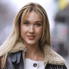 Uśmiechnięta blondynka w brązowej kurtce ze sztucznym futrem, przypominającej strój diablicy, pozuje do zdjęcia.