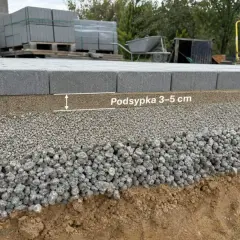 Warstwa podsypki pod krawężniki o grubości 3-5 cm, ułożona na kruszywie, zapewnia stabilność nawierzchni.