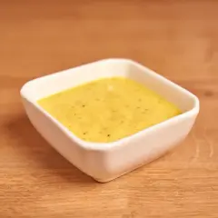 Un cuenco blanco contiene una cremosa salsa miel y mostaza, lista para acompañar tus platos.