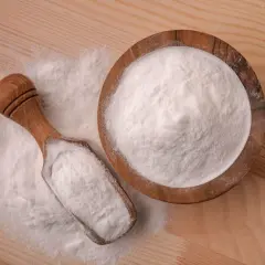 Biały proszek w drewnianej misce i łopatce na drewnianym tle.