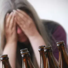 Verzweifelte Frau mit Händen vor dem Gesicht, umgeben von Bierflaschen. Ein Symbol für die Gefahren von Alkohol und die mögliche Entwicklung von Alkohol-Demenz.
