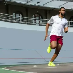 Czarnoskóry sportowiec w czerwonych spodenkach i żółtych butach biegnie po bieżni. Czy to najszybszy człowiek świata km/h?