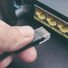 Main d'une personne tenant un câble rj45, prêt à le brancher dans un routeur. Connexion réseau.