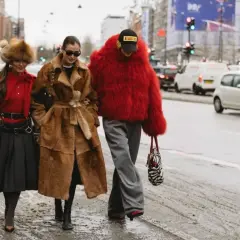 Tre kvinnor i trendiga ytterkläder, en med röd pälsjacka, visar upp **copenhagen street style** på en snöig gata.