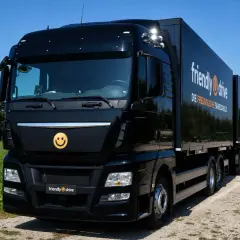 Schwarzer Lkw mit Anhänger, Werbung für "friendly drive - Die freundliche Fahrschule". Ein Smiley-Logo ziert die Front.