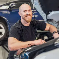 Glad mekaniker arbetar med en b1 service på en Mercedes. En blå bil syns i bakgrunden.