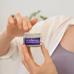 Hände halten ein Glas "RE-ENERGIZING SLEEPING CREAM". Für jugendliche Haut braucht man eine Nachtcreme.