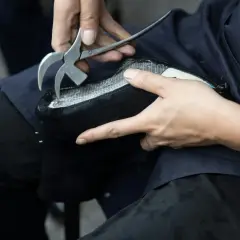 Mains expertes utilisant un outil pour réparer le simili cuir qui s'effrite sur un objet noir.