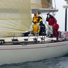 Equipaggio su una barca a vela, con un uomo che sembra D'Alema in giacca gialla.