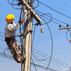 Elektryk w żółtym kasku pracuje na słupie energetycznym, podłączając kable. Zastanawiasz się, ile kosztuje przyłącze prądu?