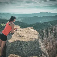 Une femme profite d'une vue panoramique sur les Vosges lors d'un trek. Les montagnes s'étendent à perte de vue sous un ciel nuageux.