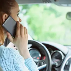 Kobieta rozmawia przez telefon podczas jazdy samochodem, ignorując drogę.