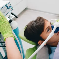 Chłopiec w masce z gazem rozweselającym, dentysta reguluje aparat.