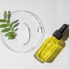 Kropla serum z **retinolem na zaskórniki** obok zielonej gałązki i białego kremu w szalkce Petriego.
