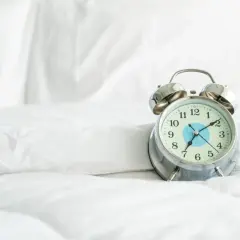 Budzik na białej pościeli.