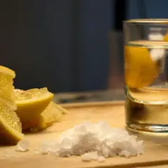Składniki na vodka sour przepis: kieliszek wódki, cytryna i sól na desce.