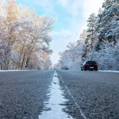 Droga przez zaśnieżony las. Czarny lód na jezdni, drzewa pokryte szronem. Samochód jedzie w stronę widza.