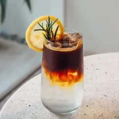 Orzeźwiający tonic espresso z plasterkiem cytryny i rozmarynem, idealny na upalny dzień.