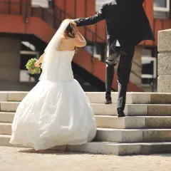 Un couple monte les marches, la mariée en robe blanche tenant un bouquet, le marié en costume noir. Une scène symbolisant leur union, peut-être après une lettre mariage mairie.