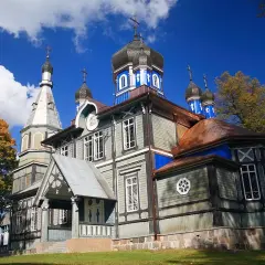 Drewniana cerkiew z błękitnymi kopułami i krzyżami, otoczona jesiennymi drzewami. Jedna z wielu pięknych cerkwi w Polsce.