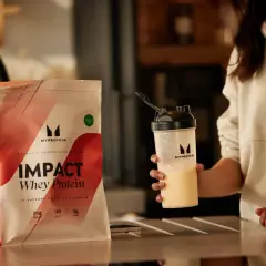 Eine Person hält einen Shaker mit einem cremigen Getränk. Daneben liegt eine Packung Myprotein Impact Whey Protein. Perfekt für den proteinshake vor dem schlafen.
