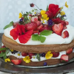 Enkel tårta med vispgrädde, jordgubbar och vilda blommor på ett silverfat.
