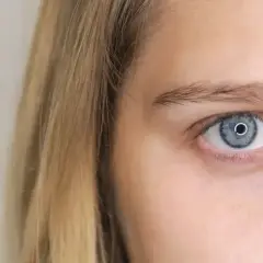Jasne, niebieskie oko z wąskimi źrenicami, otoczone blond włosami.