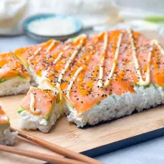 Rechteckige sushi rollen ohne matte, belegt mit Lachs, Avocado und Mayonnaise, bestreut mit Sesam.
