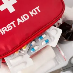 Czerwona apteczka z napisem "FIRST AID KIT", tabletki, bandaże, buteleczka z płynem i maski.