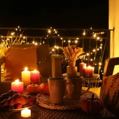 Przytulny balkon z jesienne dekoracje diy: migoczące lampki, dynie, świece i gorące napoje.