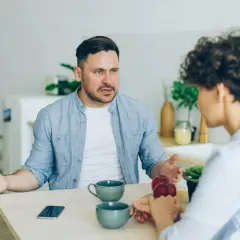 Mężczyzna z wyrzutem mówi do kobiety, która zdaje się ignorować narcyza, skupiając się na jabłkach.