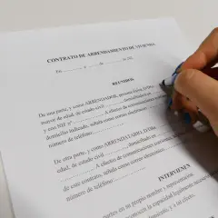 Mano con bolígrafo firmando un contrato de arrendamiento de vivienda. Se detallan los requisitos para alquilar un piso como propietario.