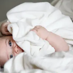 Niebieskooki maluch wtulony w biały kocyk. Czas zacząć naukę, jak oduczyć dziecko pampersa, ale na razie odpoczynek.