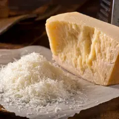 Un pezzo di Parmigiano Reggiano accanto a una montagnetta di formaggio grattugiato. Si può congelare il parmigiano grattugiato per averlo sempre pronto.